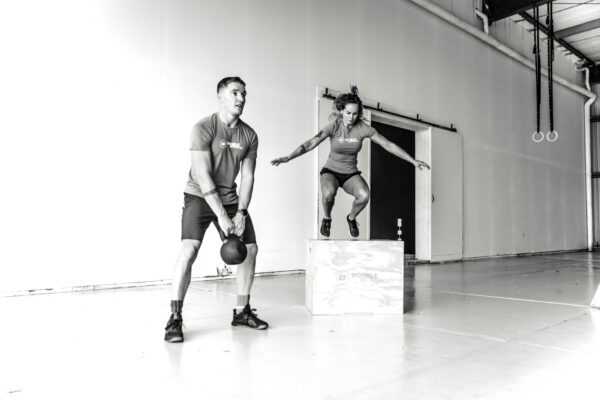 box jump en een kettlebell swing uitgevoerd op een houten plyo box en met een 24kg kettlebell door een vrouwelijke en mannelijke crossfit atleet