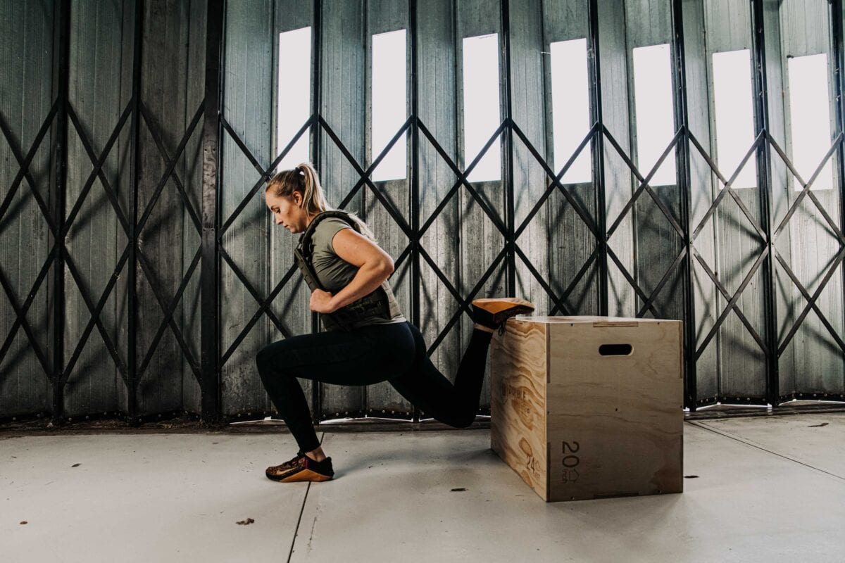 Bulgarian split squat met een gewichtsvest in de kleur goren van 6kg op een plyo box door een vrouwelijke crossfitter