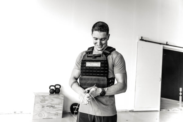 crossfit atleet die een zwart gewichtsvest draagt en een speed rope in zijn handen houdt, voor een houten plyo box